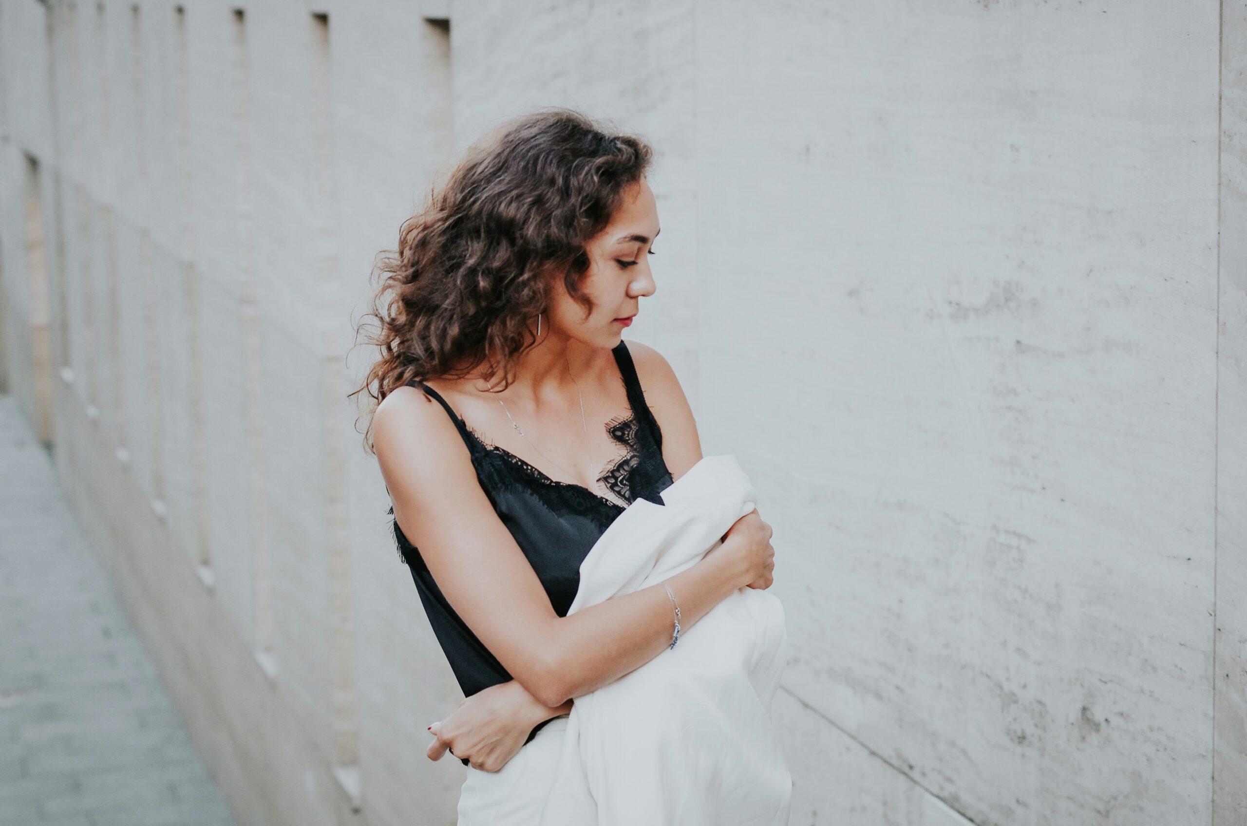Woman in a black tank top wrapping a white jacket around her arms and looking down