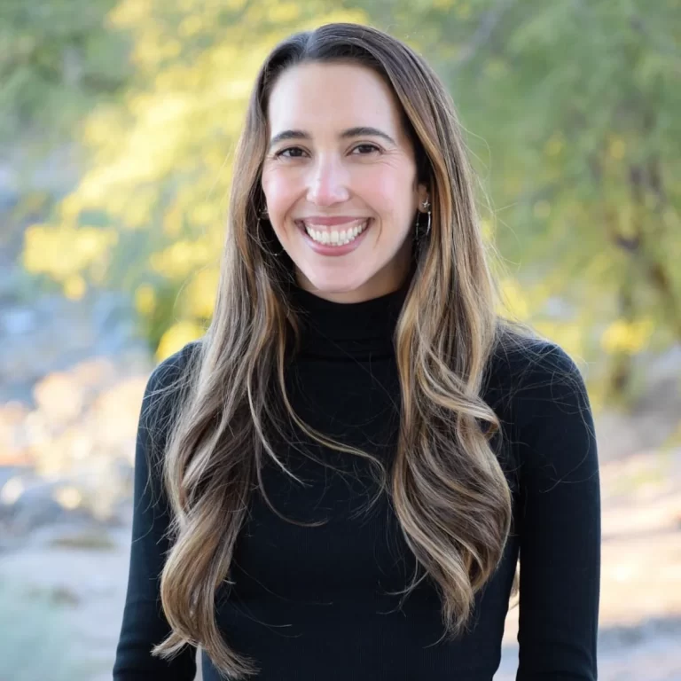 Woman with long brown hair wearing a black turtleneck smiling at the camera